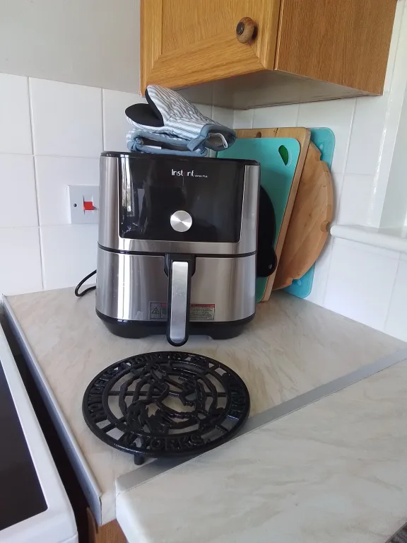 Instant Vortex Plus 6 Qt sobre la meseta de una cocina real, junto a agarraderas de horno y tablas de cortar