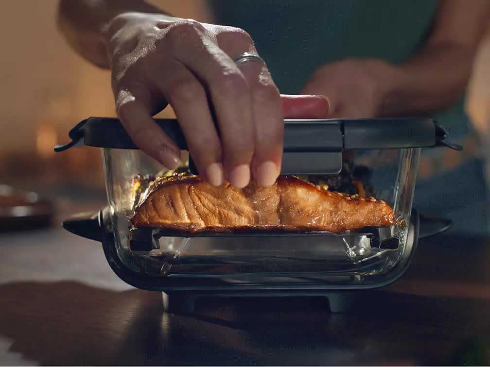 Mano colocando un filete de salmón dentro de uno de los contenedores de vidrio del Ninja Crispi, como referencia de tamaño